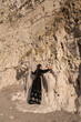 © Milou Dirks - art portrait of asian girl in long vintage black dress leaning against large cliff wall of rocks  in nature