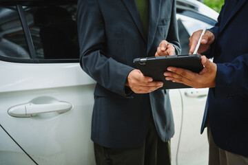 Wall Mural - Two Asian individuals discuss a car insurance claim with an agent in front of a damaged vehicle. They review documents, discuss the policy, and address the crash and repair costs.