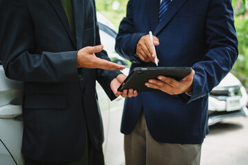 Wall Mural - Two Asian individuals discuss a car insurance claim with an agent in front of a damaged vehicle. They review documents, discuss the policy, and address the crash and repair costs.