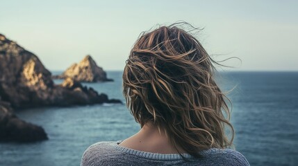 A woman with long hair is looking out at the ocean