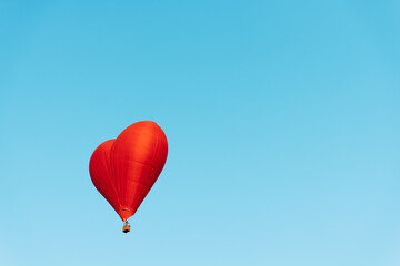 vibrant red heart shaped balloon soaring against clear blue sky background