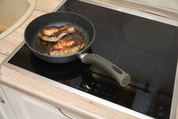 Two pieces of cooked meat in a frying pan on an induction stove. Close-up kitchen photography.