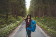 © Fauren - View of a woman with a blue backpack walking barefoot down a peaceful forest road, surrounded by lush greenery and tall trees, symbolizing adventure and tranquility in nature