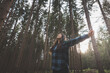 © Fauren - Happy woman in a plaid shirt with outstretched arms enjoying the serenity of a dense forest, surrounded by tall trees, feeling freedom and connection with nature