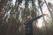 © Fauren - Happy woman in a plaid shirt with outstretched arms enjoying the serenity of a dense forest, surrounded by tall trees, feeling freedom and connection with nature