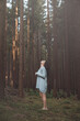 © Fauren - Serene woman in a cozy grey sweater stands barefoot in a tranquil forest, gazing upwards with a peaceful expression, capturing a moment of connection with nature and inner calm