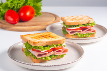 Close-up of two sandwiches with bacon, salami, prosciutto and fresh vegetables on rustic wooden cutting board. Club sandwich concept