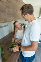 Wall Mural - Family with a young father and his little daughter preparing greens for a healthy juice or smoothie in home kitchen