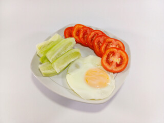 A sunny side up egg, paired with fresh slices of tomato and cucumber, neatly arranged on a square white plate against a white background, offering a simple yet nutritious meal presentation