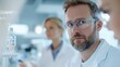 © justjupiter - Focused scientist in laboratory, wearing glasses, analyzing samples with colleagues in the background, showcasing modern research.