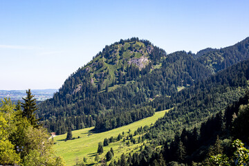 Scenic view of lush green mountains under clear blue skies in the Bavarian Alps during late spring, showcasing vibrant valleys and rocky peaks