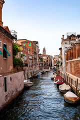 Wall Mural - Quiet Venetian canal lined with colorful buildings under a clear sky, showcasing boats and a small stone bridge during the day