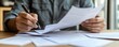 © Sodapeaw - Close-up of a person working with documents, analyzing paperwork, and writing notes at a desk. Concept of office work, paperwork, and administration.