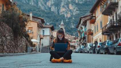 Poster - A young woman sits on the street in front of her laptop, surrounded by old buildings and cars parked on both sides of an empty mountain road
