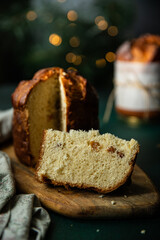 Two homemade Christmas panettone , one cut and the other whole, made as holiday present with pine and red berries decorations with Christmas lights on green background.