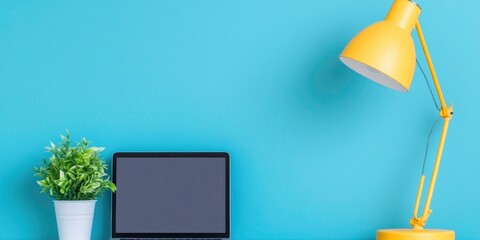 An attractive desk lamp, a compact potted plant, and a slim laptop are arranged next to a modern desk to create a functional and welcoming workstation.