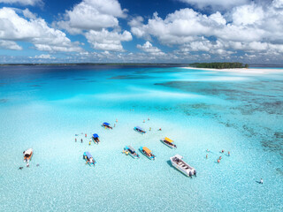 Canvas Print - Aerial view of colorful boats in clear azure water in summer. Mnemba island, Zanzibar. Top view of sandbank in low tide, blue sea, white sand, swimming people, yachts, dramatic sky with clouds. Ocean