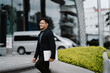 © Wicitr - Confident Stride: A young businessman exudes confidence and ambition as he confidently walks towards his future, laptop in hand. His stylish attire and bright smile suggest an optimistic and successfu