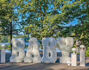 Baby shower or gender reveal decoration. Letters with word baby made of flowers on the shore of lake - decor for newborn celebration