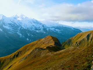 Wall Mural - mountainous landscape with verdant mountain slope in front of bare snow-capped mountain peaks in aut