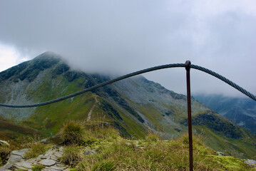 Wall Mural - mountainous landscape with a steel wire fence in front of a high mountain peak a cloudy day in autum
