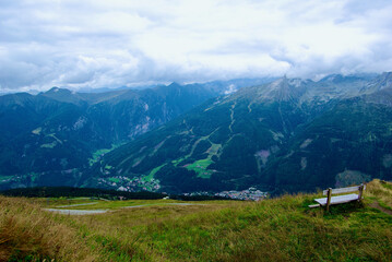 Wall Mural - a wooden bench with a view of an amazing mountain landscape on a hazy day with gray clouds and fog o