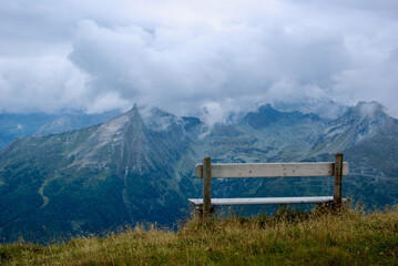 Wall Mural - close-up of a wooden bench with a view of an amazing mountain landscape on a hazy day with gray clou