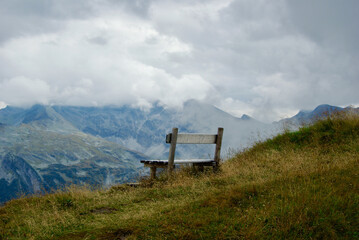 Wall Mural - close-up of a wooden bench with a view of an amazing mountain landscape on a hazy day with gray clou