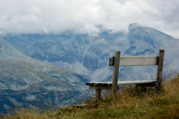 Wall Mural - close-up of a wooden bench with a view of an amazing mountain landscape on a hazy day with gray clou