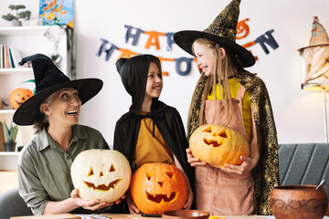 Wall Mural - Mature woman and little girls wearing witch hats holding carved pumpkins celebrating halloween