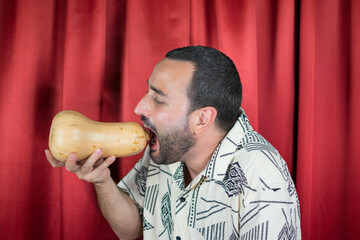 Funny young adult man with white shirt playing with Pumpkin and biting it