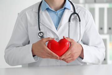 Wall Mural - Doctor with red heart at white table in clinic, closeup