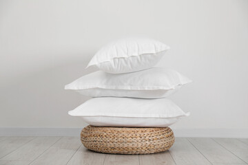 Wall Mural - Stack of clean pillows on wicker pouf near white wall