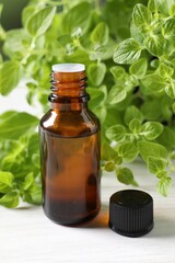 Poster - Essential oil in bottle and oregano leaves on white wooden table, closeup