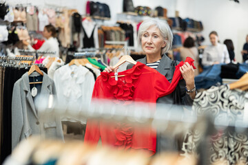 Canvas Print - Elderly woman buyer chooses blouse in clothing store..