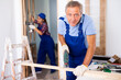 © JackF - Concentrated male builder in uniform using a jigsaw machine on wooden plank at the apartment