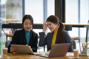 Two young Asian businesswomen discussed investment project work and planning strategy. Business people talk together on laptop computers at the office.