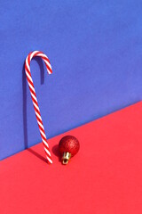 On a blue and red background there is a cane and a Christmas tree toy.