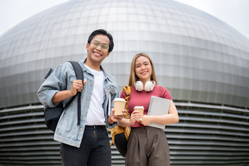 Wall Mural - Two happy young Asian college students are standing outdoors on campus and smiling at the camera.