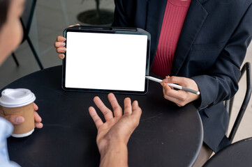 A digital tablet with a white screen mockup on a table during the meeting with two businesspeople.