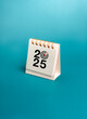 © tete_escape - Happy new year 2025, vertical banner. 2025 number with target icon on small desk calendar cover, isolated on blue background, minimal style. Business plan agenda, mission and success goal concept.