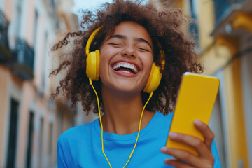 Canvas Print - A happy woman with a yellow mobile phone and headphones is dancing in the street while listening to music, wearing a blue shirt.