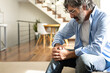 © Daniel - Mature man having knee pain sitting on the sofa at home living room. Copy space.