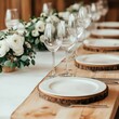 © Natthapat - Rustic wedding table arrangement featuring wood slice chargers, white plates, wine glasses, and floral decor with white flowers.
