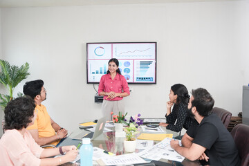 Young indian woman at discussing company future growth to team members or colleagues in conference room. Start up, leadership and workplace concept.