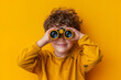 © MuhammadAwais - 10-year-old boy looking through a pair of binoculars, happy, on a yellow background