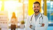 © Yuparet - A cheerful male doctor with a stethoscope around his neck, standing confidently in a brightly lit hospital environment.