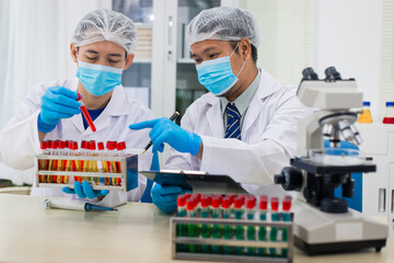 A modern laboratory scene showcasing scientists, both male , in lab coats, analyzing samples using microscopes and computers.