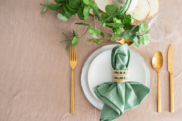 Table setting for elegant festive dinner with white porcelain plates, glass, green napkin, gold cutlery and centre place. Copy space