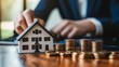 © fotofabrika - Real estate investment strategy involving a model house and stacked coins during a meeting in a modern office